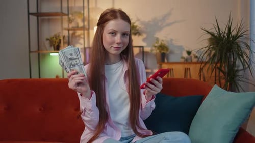 Girl Holds Money and Cellphone on Couch