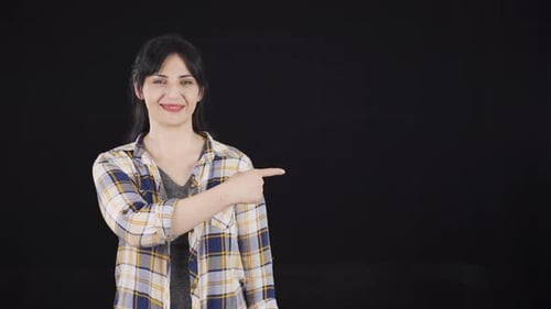 Smiling Woman Points to Side on Black Background