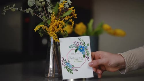 Slow Motion Closeup A Woman's Hand Places a Handmade Mother's Day Card Near a Bouquet of Spring