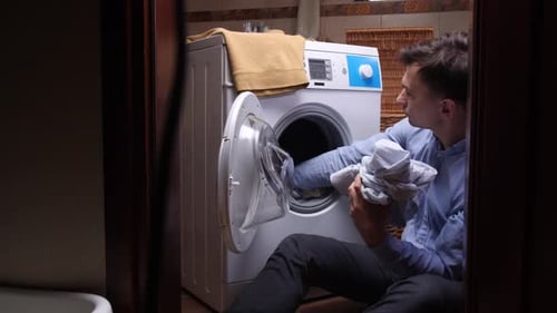 Young Man Loading Clothes Into Washing Machine