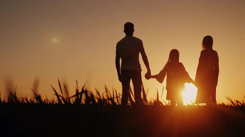 A Happy Family of Three People Meets the Dawn in a Picturesque Place Holding Hands