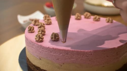 Close up following pastry nozzle as confectioner woman decorates delicious cream cake with chocolate