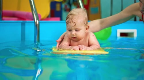 Beautiful blue-eyed Caucasian baby lies on the board in the swimming pool.
