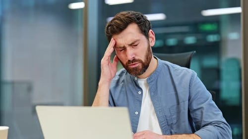 Stressed Businessman Suffering From Headache While Working on Laptop in Office