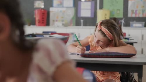 Focused diverse schoolgirls writing at desks in elementary school class, slow motion