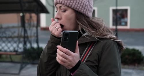 Portrait of Mature Woman in Wool Hat Standing on the Urban Street with Mobile Phone in Hand