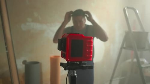 Man in Blue Construction Overalls and Goggles Adjusts Red Laser Roulette with Flashing Green Beam