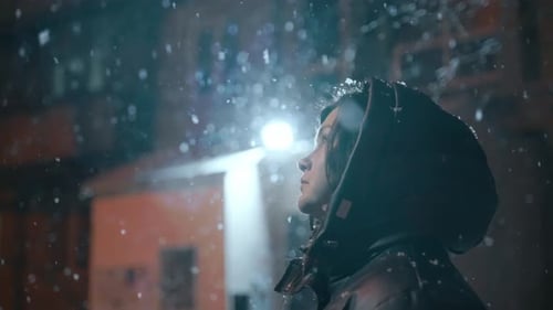 A Girl Standing Under a Street Lamp at Night Looks at the Falling Snowflakes
