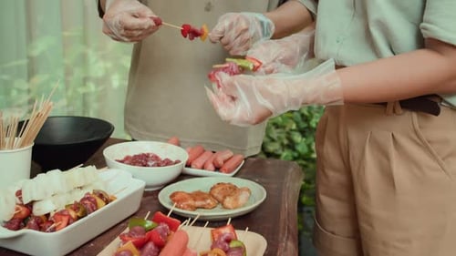 Individuals Preparing Skewers with Meat and Vegetables