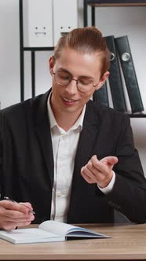Young Businessman Looking to Camera and Writing Down on Diary in Video Chat at Home Office Desk