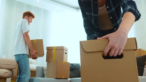 Close Up of Positive Young Man and Woman in Room with Many Boxes Putting Stuff on Floor