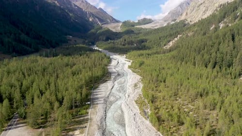 Aerial 4k Drone footage over an alpine river valley. The drone flies over pine forests and the glaci