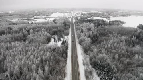 Drohnenaufnahme von Autos, die auf einer zweispurigen Autobahn durch eine gefrorene Winterlandschaft mit vereistem T fahren