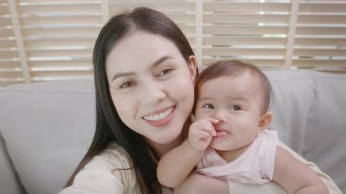 Smiling Young Adult Woman Holding Infant On Couch