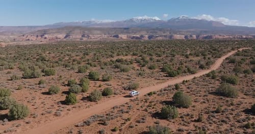 Wide aerial following vehicle across vast desert landscape on rugged remote road
