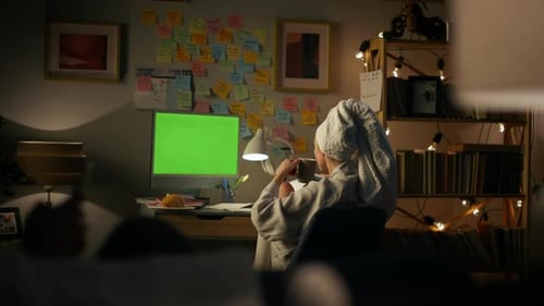Unbekannte Frau im Bademantel genießt Tee und Greenscreen-Computer zu Hause