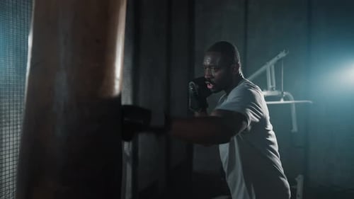 Boxer Training Hitting Punching Bag African American Sweated Sportsman Practicing Punches in Gym