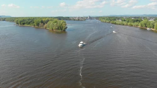 4K aerial descending footage of a small yacht cruising down a large river with a split in the river