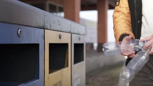 A man throws a plastic empty bottle into a trash bin for recycling.