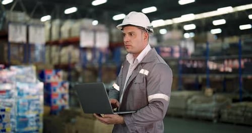 caucasian male warehouse operator reviewing supply chain data on laptop while standing alone in