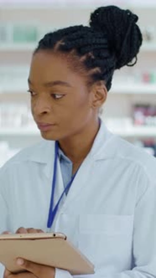 African American Beautiful Woman Pharmacist with Braids Using Tablet Computer Examining Drug