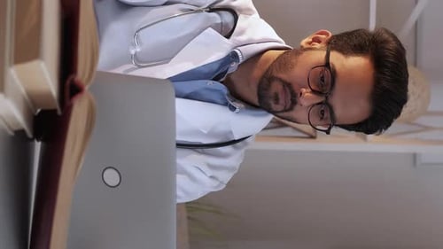 Doctor Working at Desk with Laptop and Book