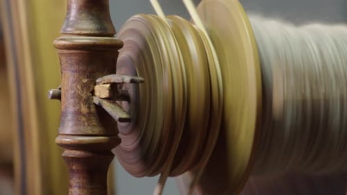 Full frame close up: Yarn bobbin spins on traditional spinning wheel