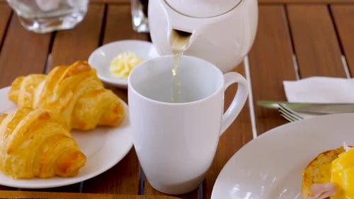 Pouring Tea With Croissants and Eggs Benedict