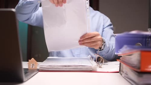 Accountant Filing Documents in Binder at Office Desk