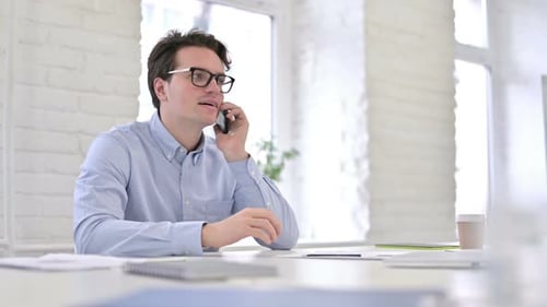 Attractive Working Young Man Talking on Smartphone in Office