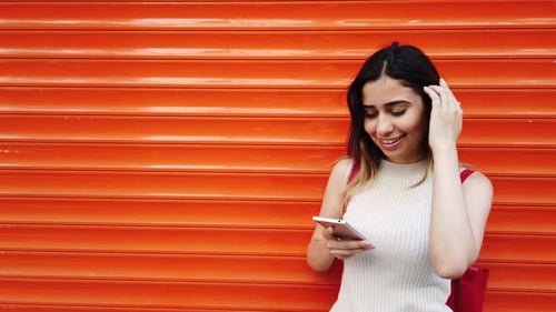 Smiling Woman Using Phone Against Orange Wall