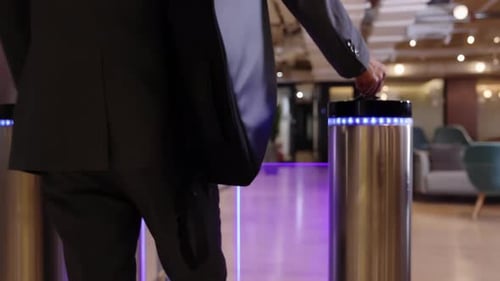 Empresário de terno carregando uma mochila caminha por uma catraca de segurança automática