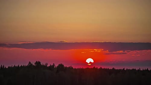 Sun dips below cloud and forest at sunset; telephoto time lapse shot