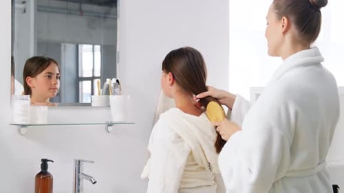 Woman brushes child's hair in bright bathroom