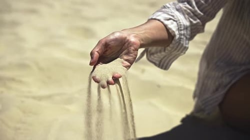 Female Hand Against Sand Background with Quartz Silicon Oxide Slowly Sifting Through Fingers