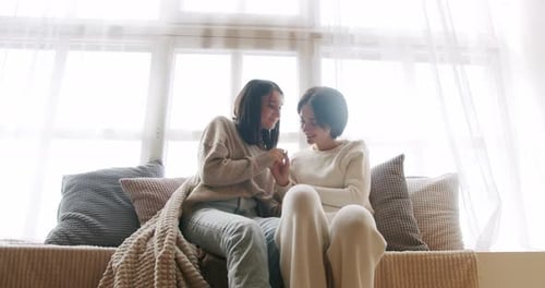 Two women sit and chat in a bright apartment