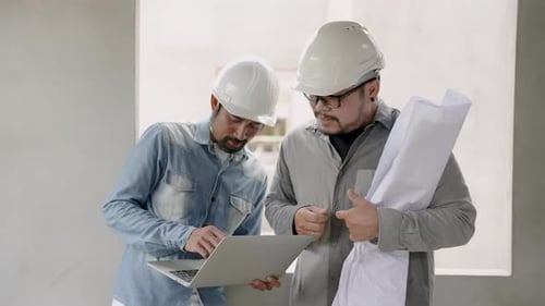 Mustachioed Indian engineer wearing hard hat standing in front of workers