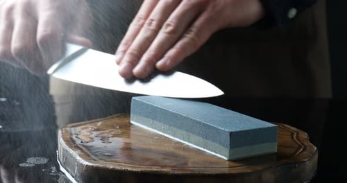 Man sharpening knife with sharpener at mirror table, closeup