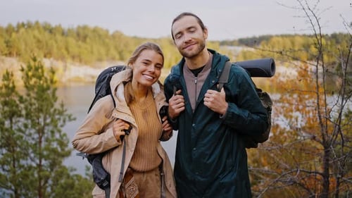 Smiling Couple with Backpacks Posing by Lake