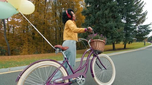 Happy Woman Walks Bike with Balloons in Autumn Park