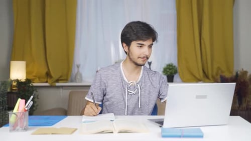 Focused Young Adult Studying with Book and Laptop