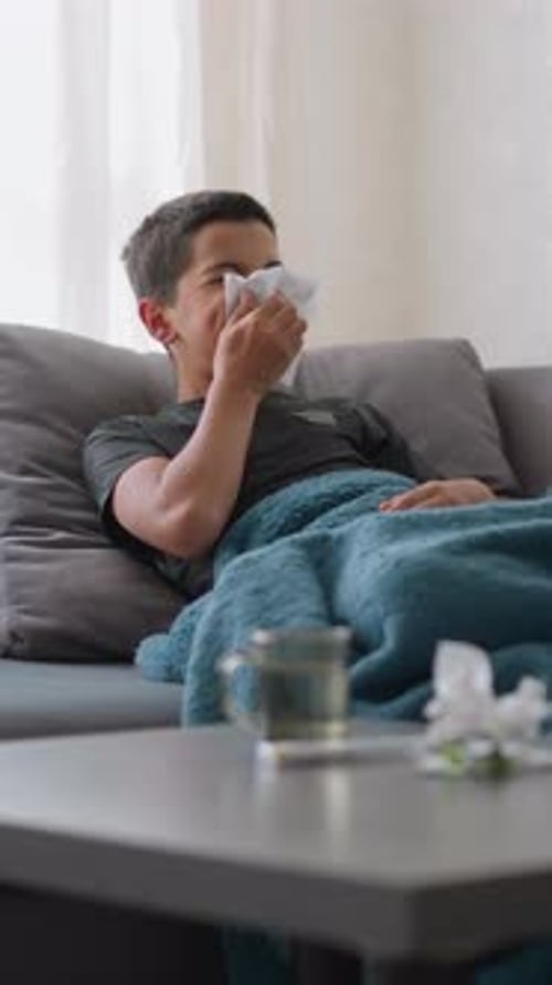 Sick Boy Lying on Sofa Blowing Nose