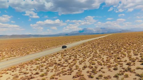 Catching up with a black car moving by the empty road through the desert.