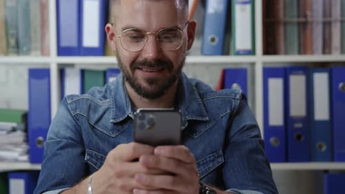 Man Uses Smartphone at Desk in Office