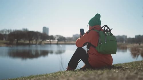 Woman Resting After Hiking in Park Sitting on Pond Shore Take Mobile Photo Active and Healthy