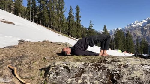 chakrasana de yoga avanzado en terreno rocoso con pendientes cubiertas de nieve