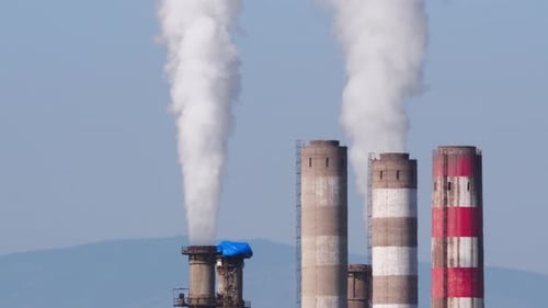 Industrial Smokestacks Emitting White Smoke Against Blue Sky