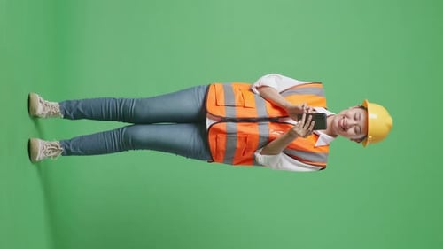 Full Body Of Asian Female Engineer With Safety Helmet Using Smartphone In The Green Screen