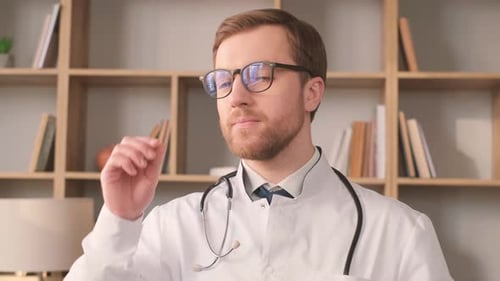 A Young Intern Doctor in a White Coat is Looking at the Camera and Smiling