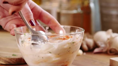 Woman's Hand Mixing Creamy Herb Sauce in a Glass Bowl